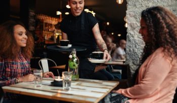 Waiter Serving Coffee To Young Women At Cafe