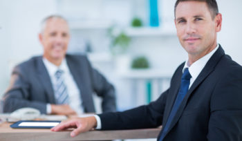 Confident businessman looking at camera with colleague behind in