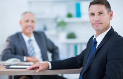 Confident businessman looking at camera with colleague behind in